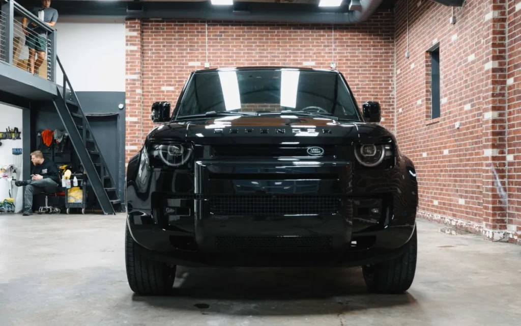 Glossy black Land Rover Defender parked inside a detailing shop after ceramic coating treatment.